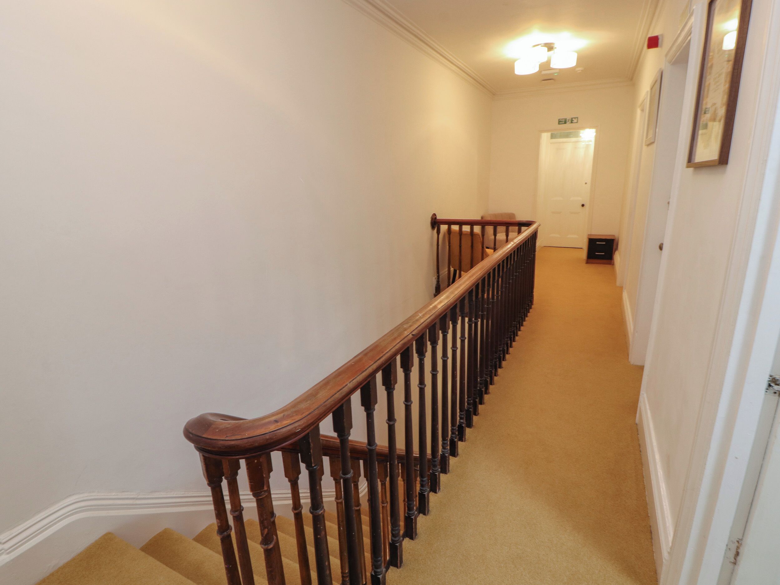 A narrow, carpeted hallway with a wooden handrail and a door at the end.