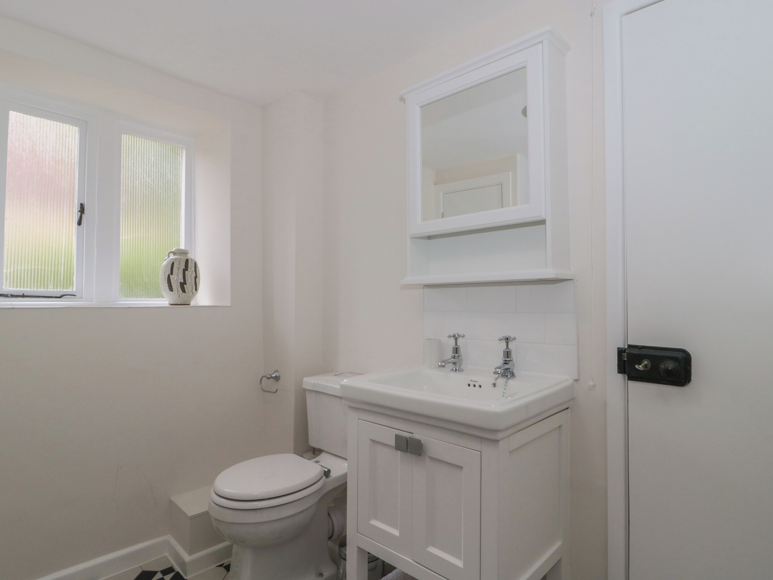 A small, white bathroom with a toilet, sink, and window.