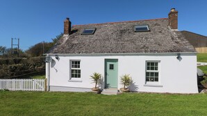 A white cottage with a green door, two windows, and a small garden. - Piglet Cottage (Haverfordwest)