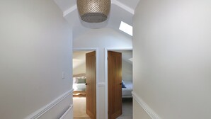 A narrow hallway with a sloped ceiling and a skylight. There are two wooden doors leading to bedrooms. - Piglet Cottage (Haverfordwest)