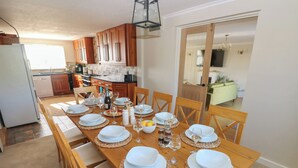 A dining table set for six with white plates and glasses, surrounded by wooden chairs. - Piglet Cottage (Haverfordwest)
