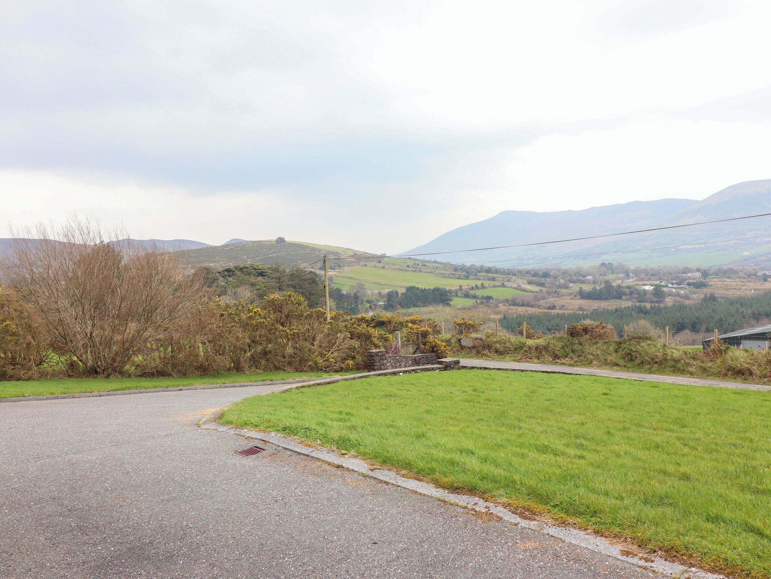 A rural road curving through a green landscape with hills in the background.