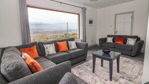 Una sala de estar moderna con un conjunto de sofá gris, una mesa de centro y vistas a un paisaje montañoso a través de un ventanal grande.