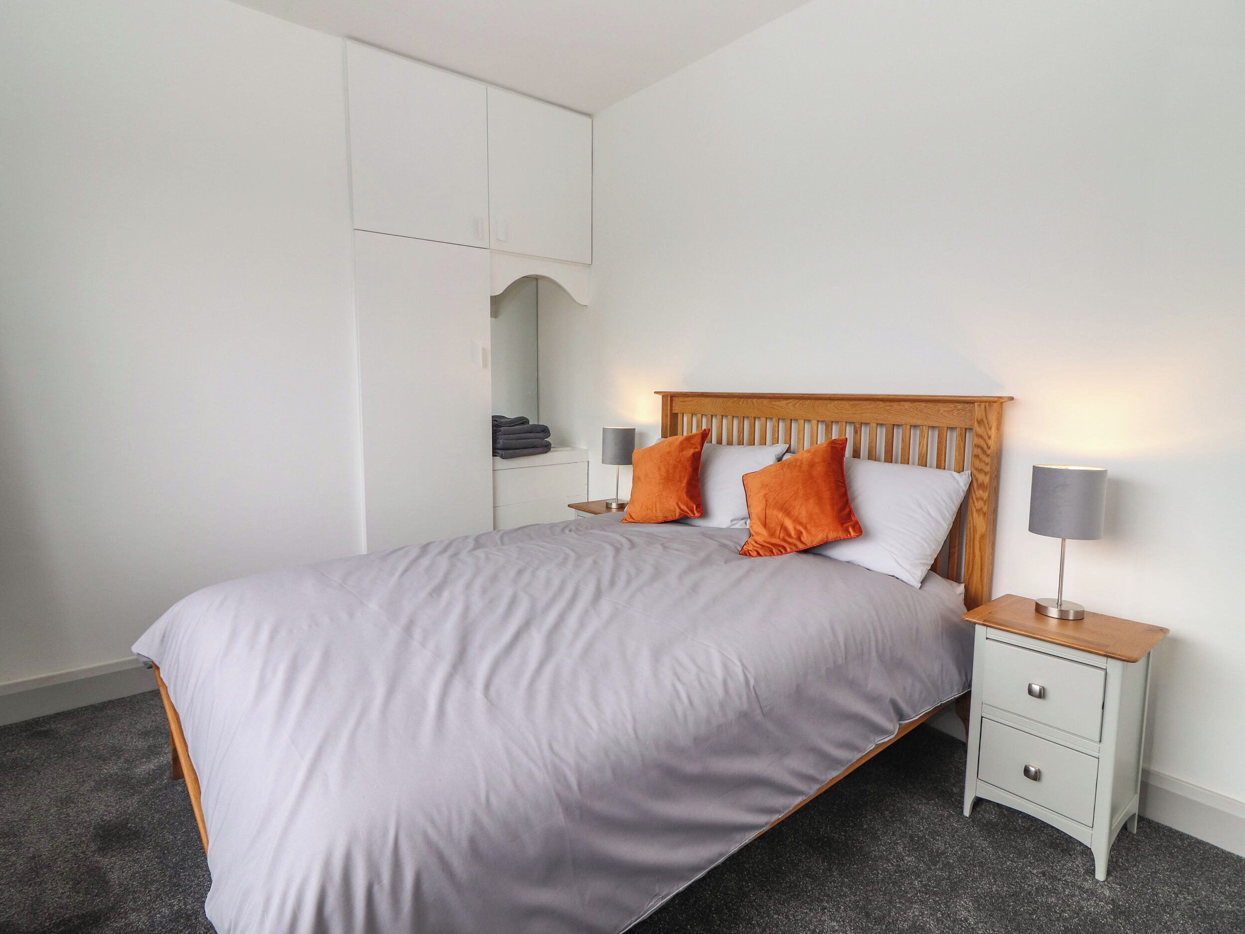 A neatly made bed with a wooden headboard, two bedside tables with lamps, and a built-in wardrobe with a mirror.