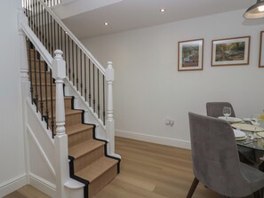 A staircase with a wooden finish and black railings, leading to a dining area with a table set for two and a chair. - Dalegarth Hall Farm Cottage 2 (Holmrook)