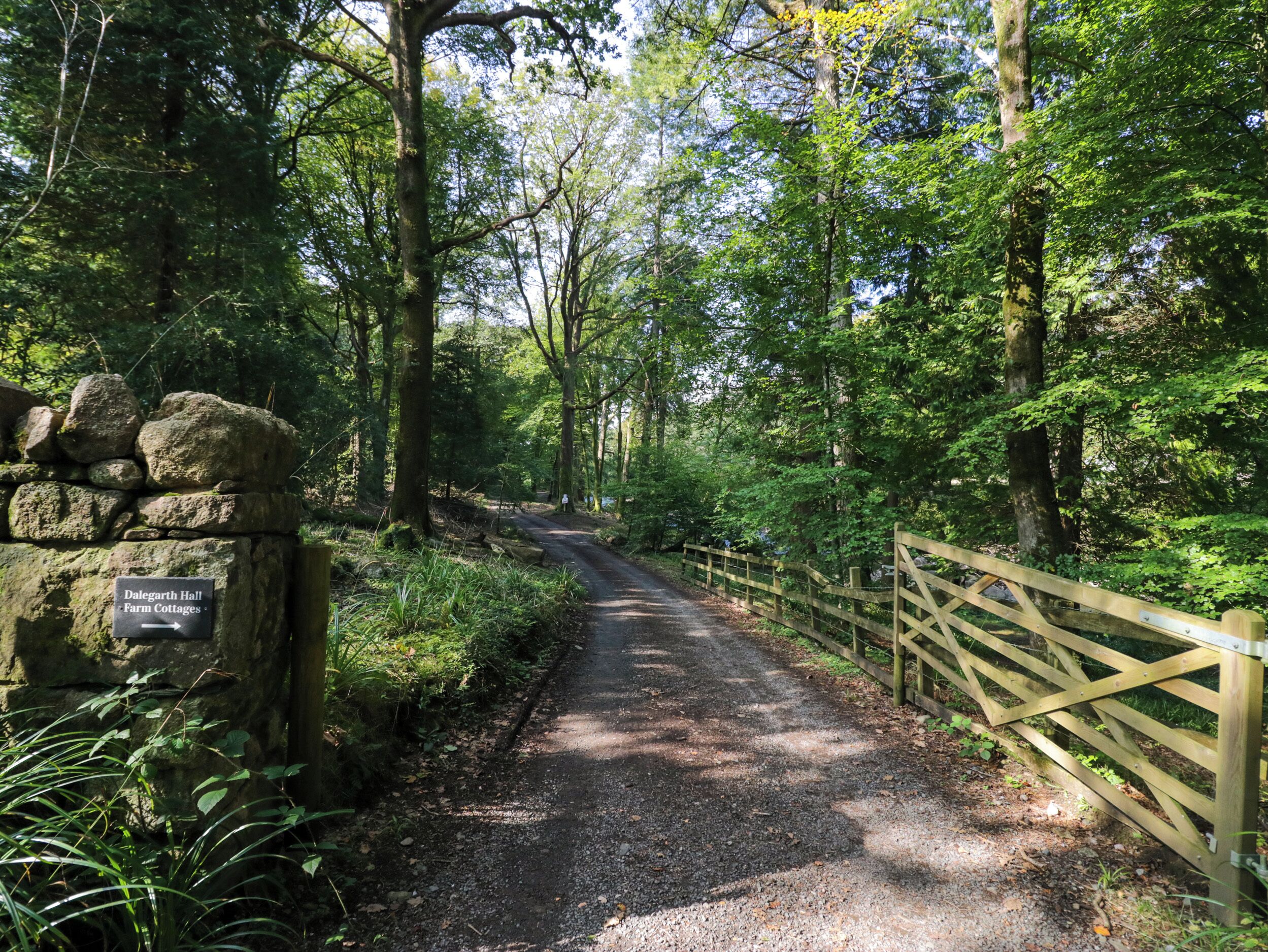 A rural road leading to a stone wall with a sign for 'Dalgarth Hall Farm Cottages'.
