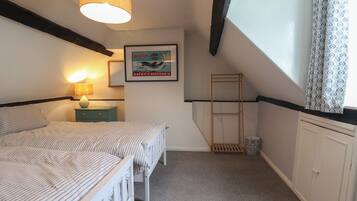A bedroom with two beds, a hanging light fixture, a framed poster, a window with patterned curtains, and a small wooden shelf.