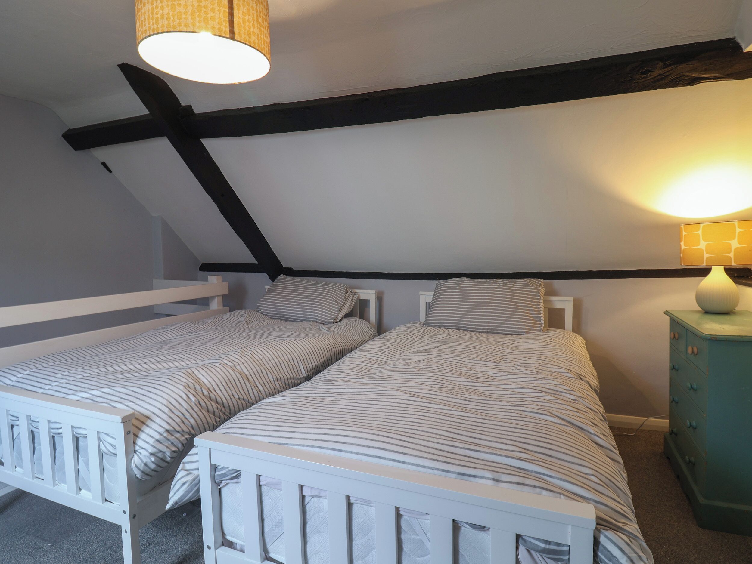 A bedroom with two single beds, a wooden ceiling, a white dresser, and a lamp.
