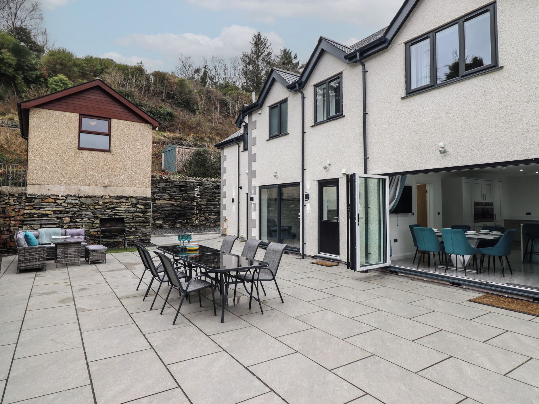 A patio with a dining table and chairs, a stone wall, and a small building with a sloped roof.