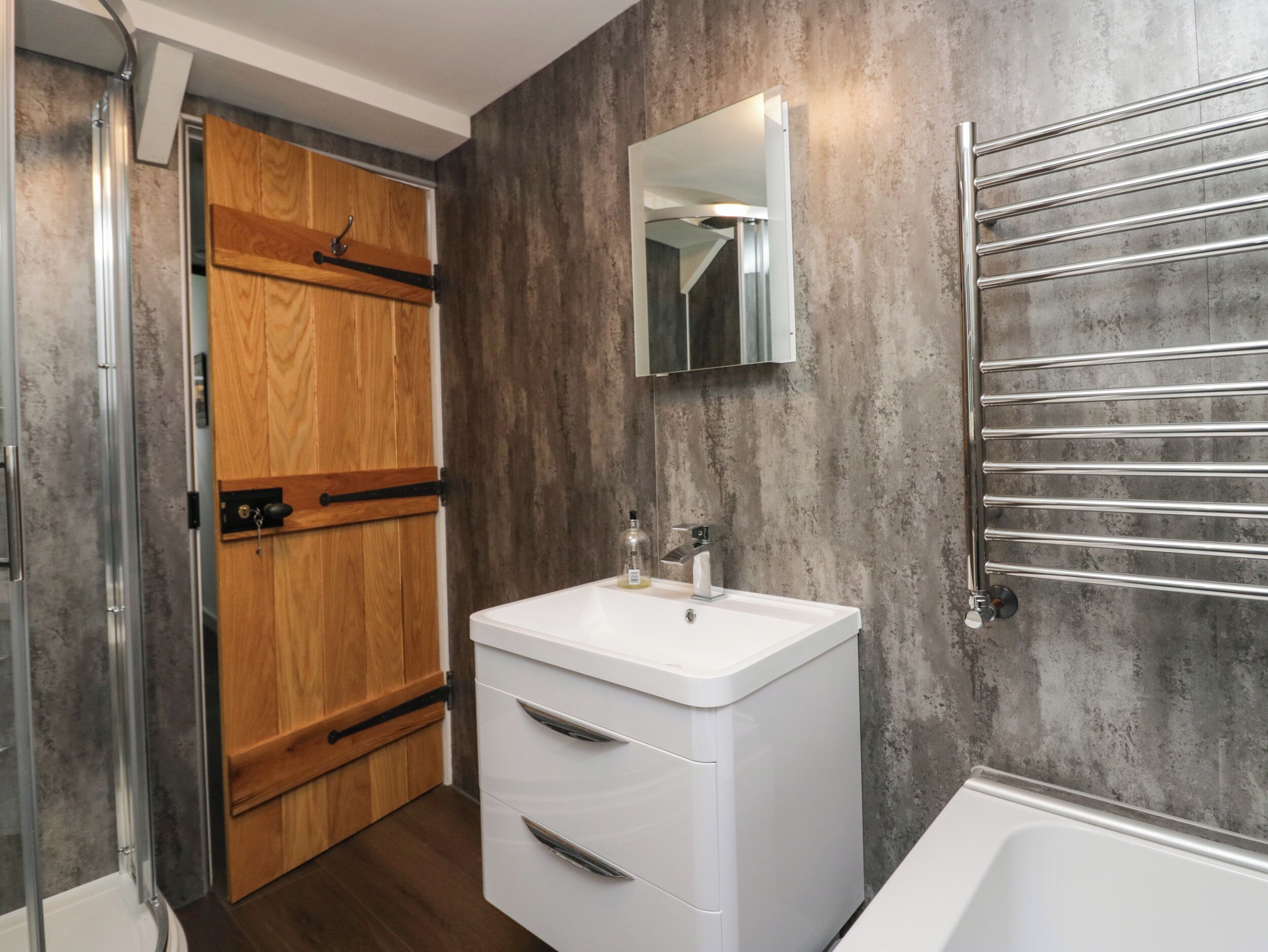 Un baño moderno con puerta de madera, lavamanos blanco, espejo y bañera.