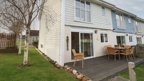 Ein zweigeschossiges Haus mit einer Terrasse, einer Glastür und einer kleinen Sitzgruppe mit Stühlen und einem Tisch.