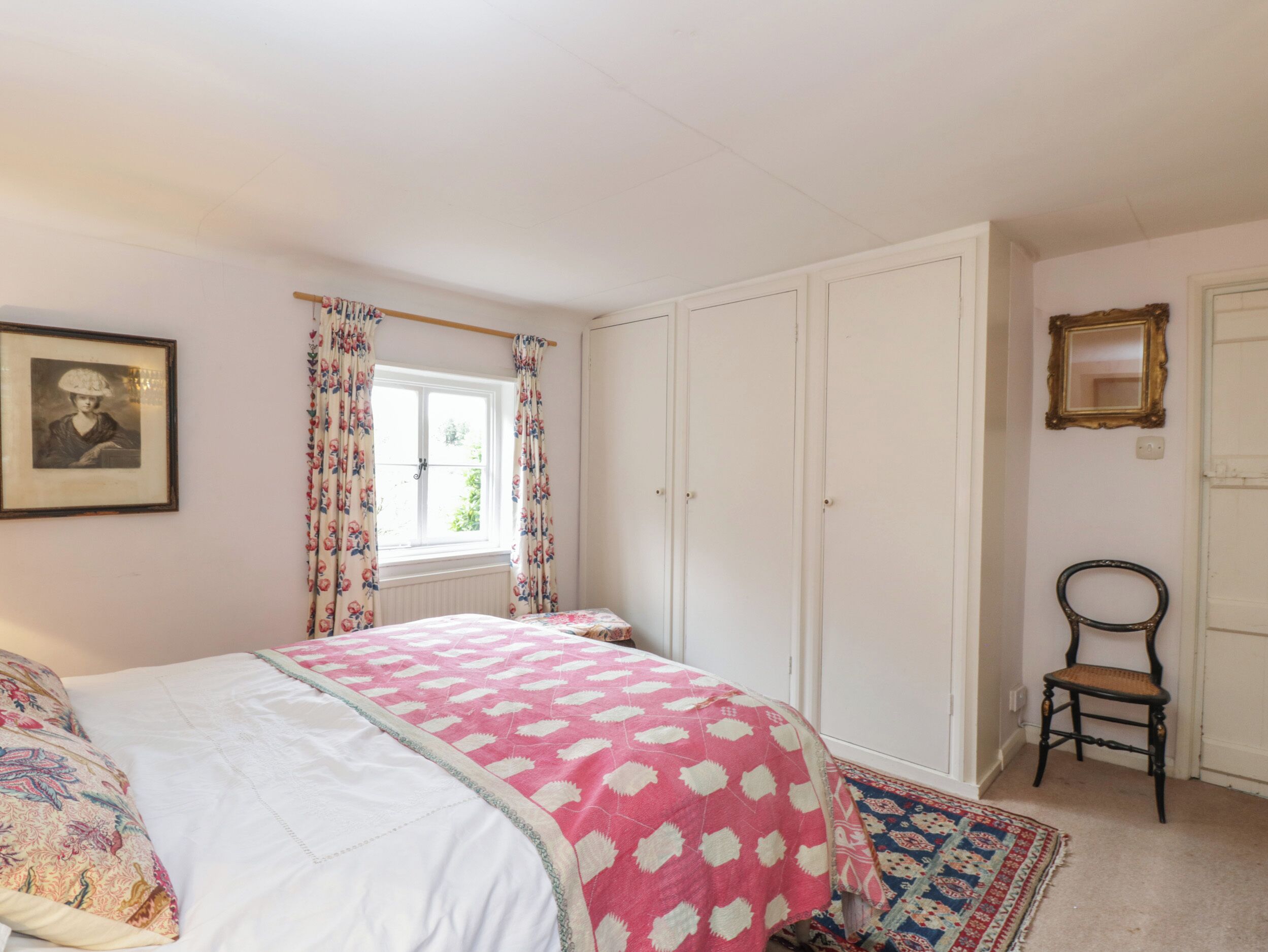 Une chambre à coucher avec un lit, une fenêtre avec des rideaux, une armoire, une chaise et un tableau encadré au mur.