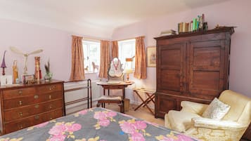 Una stanza con un letto, un armadietto in legno, una sedia, una scrivania e una finestra con tende.