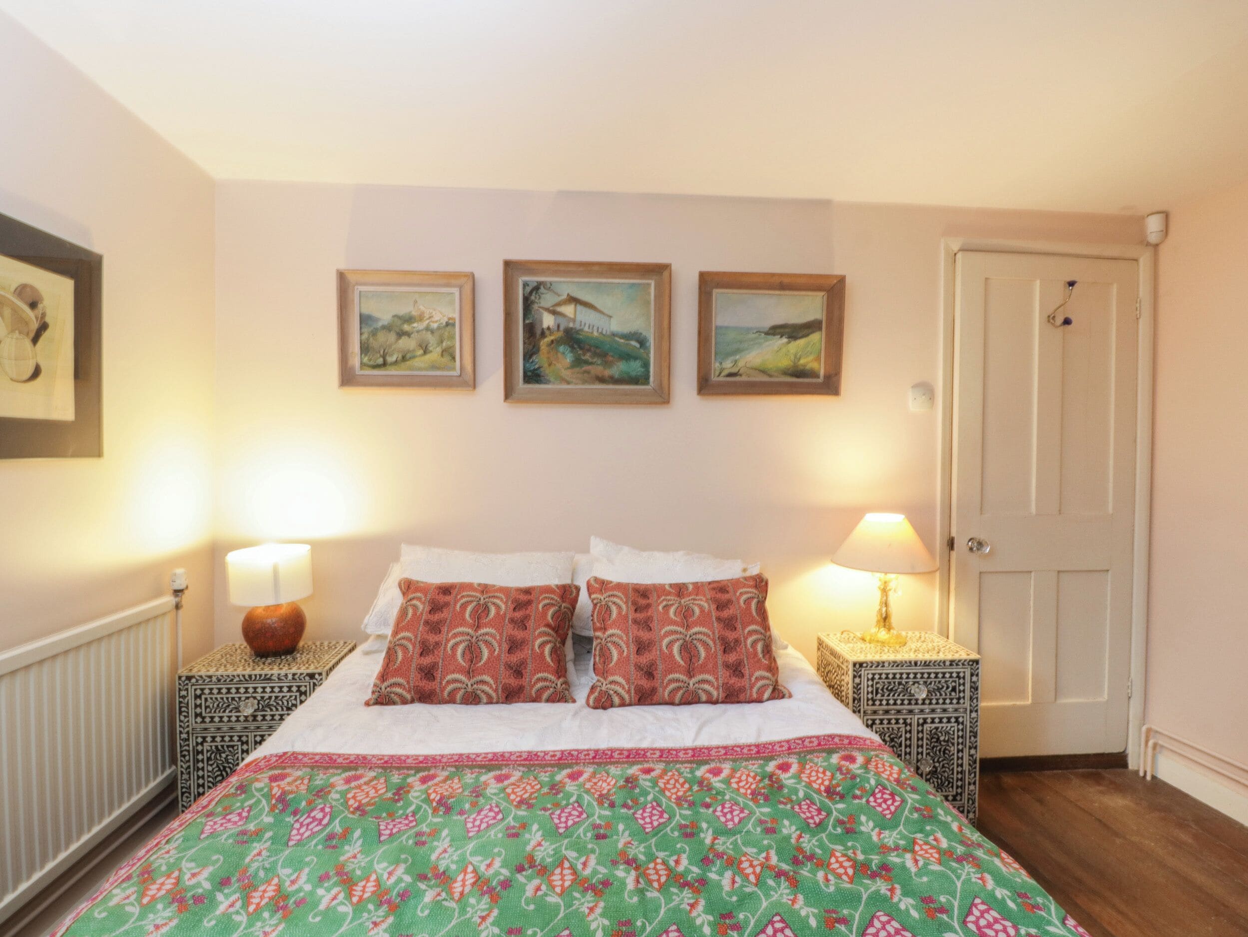 A neatly arranged bedroom with a bed, two bedside tables, a door, and three framed pictures on the wall.