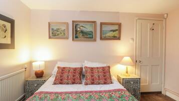 A neatly arranged bedroom with a bed, two bedside tables, a door, and three framed pictures on the wall.