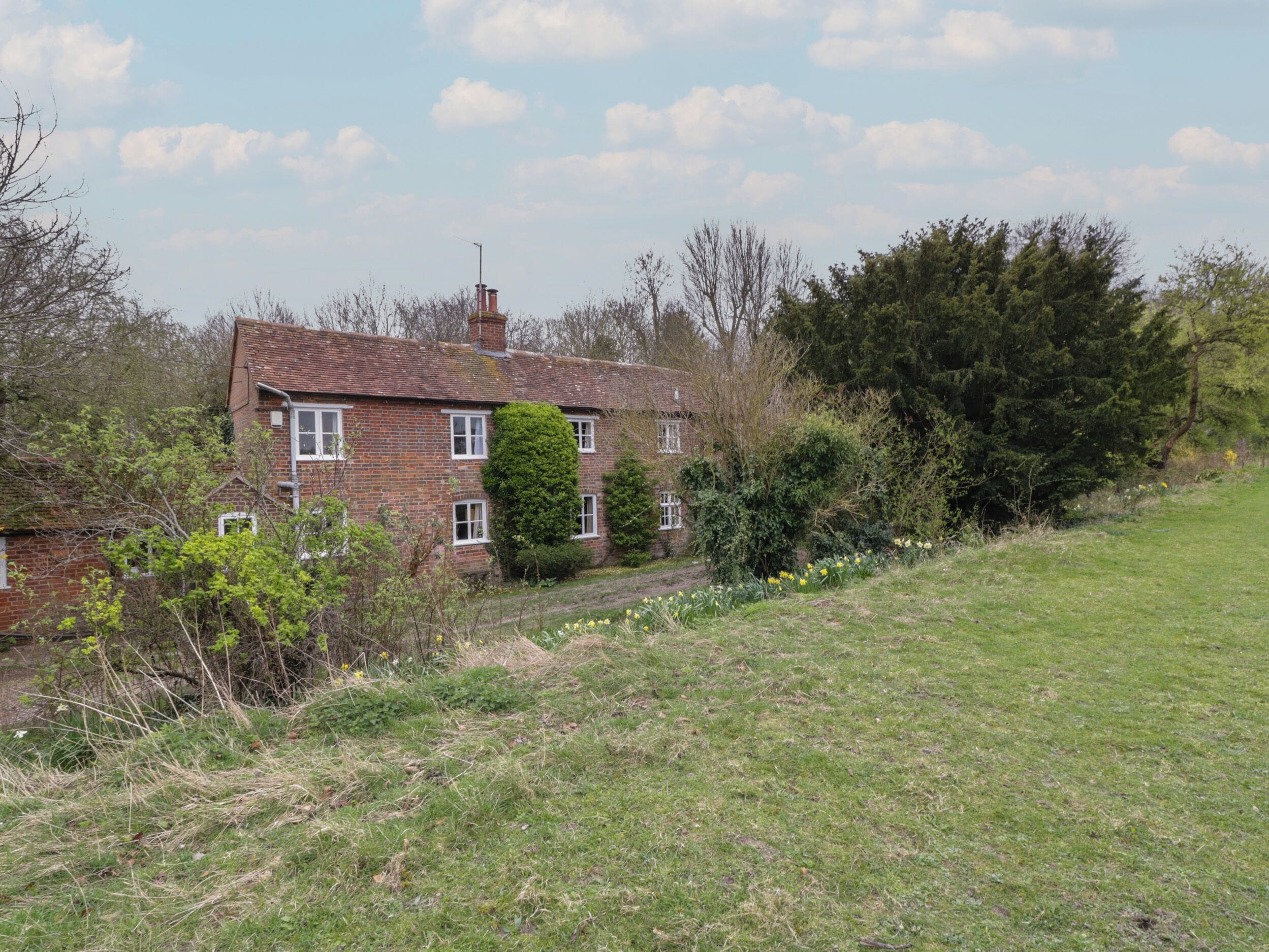 A two-story brick house with a sloped roof, surrounded by a grassy area and dense trees.