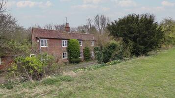 A two-story brick house with a sloped roof, surrounded by a grassy area and dense trees.