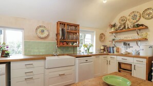 Uma cozinha com armários brancos, bancada de madeira e uma tigela verde sobre a mesa.
