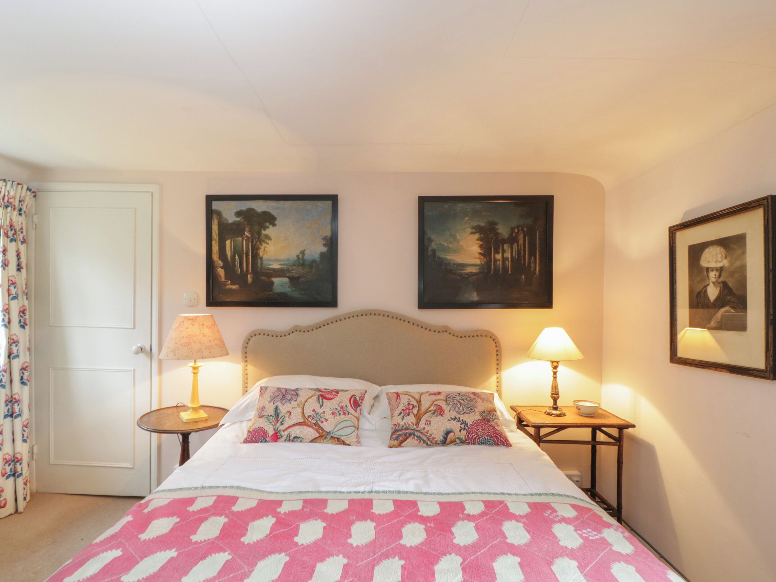 A hotel room with a bed, two bedside lamps, a small table, and two framed pictures on the wall.