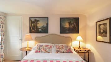 A hotel room with a bed, two bedside lamps, a small table, and two framed pictures on the wall.