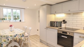 A modern kitchen with white cabinetry, a dining table with chairs, and a window with a view of greenery.