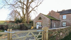 A stone building with a wooden gate, a brick wall, and a stone wall. - Luham Cottage (Penrith)