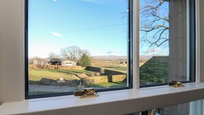 A window with a view of a rural landscape, including fields, a barn, and a tree. - Luham Cottage (Penrith)