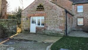 A stone building with a white door, a small window, and a brick chimney. - Luham Cottage (Penrith)