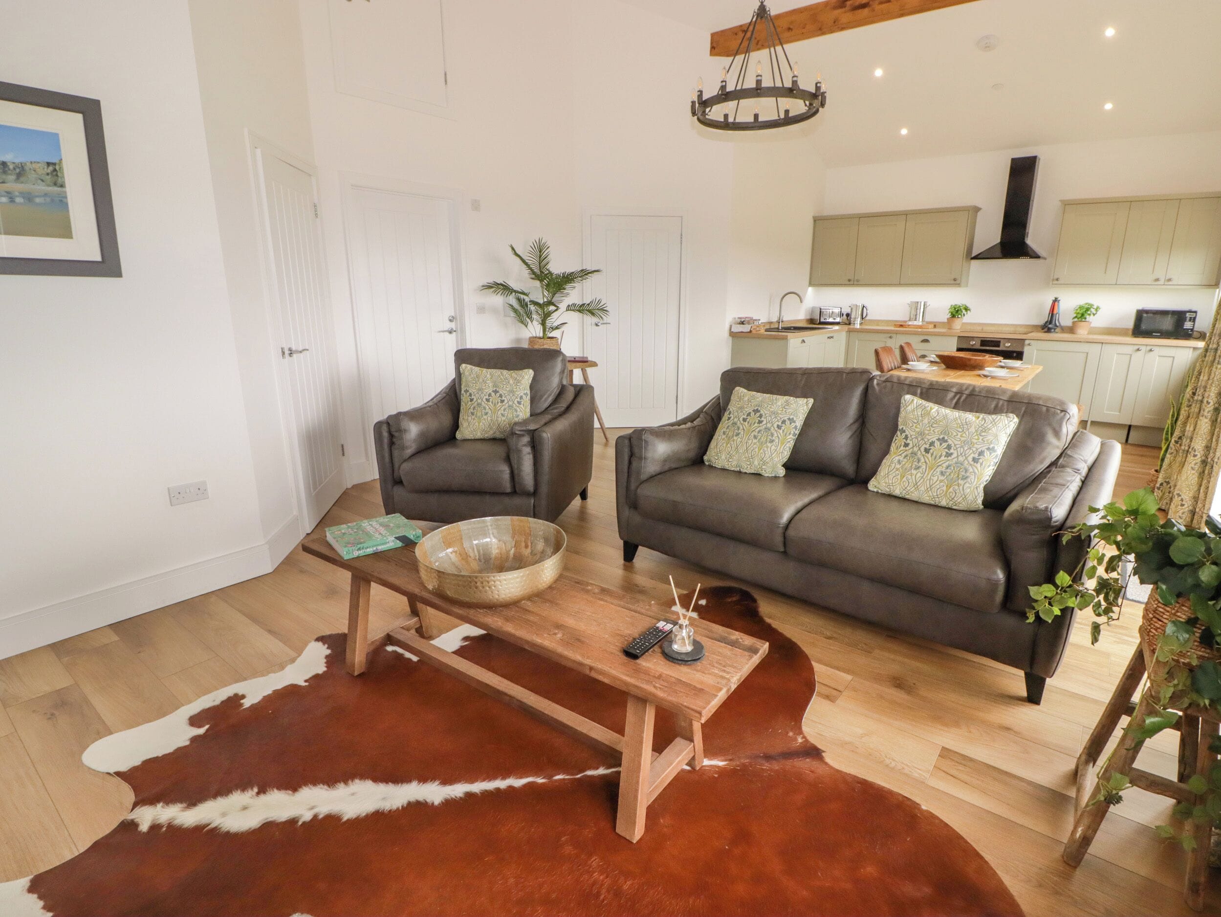 A living room with two leather sofas, a wooden coffee table, a cowhide rug, and a kitchen in the background.