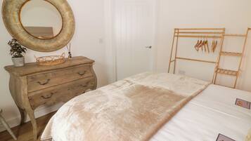 Un dormitorio con un aparador de madera, un espejo grande, una cama con edredón blanco y un cabecero de madera con ganchos.