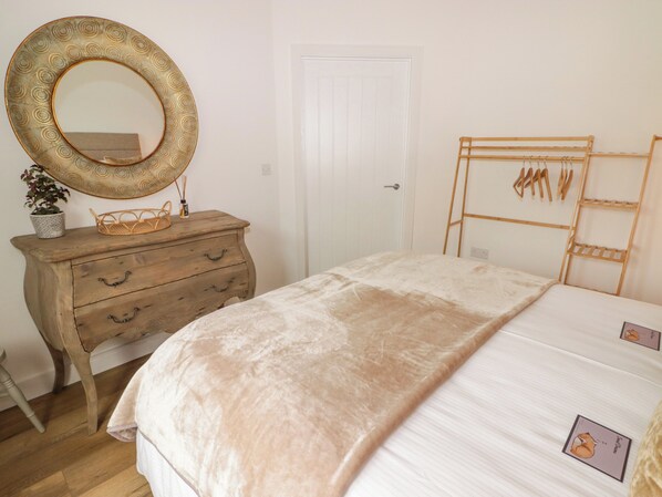 Un dormitorio con un aparador de madera, un espejo grande, una cama con edredón blanco y un cabecero de madera con ganchos.