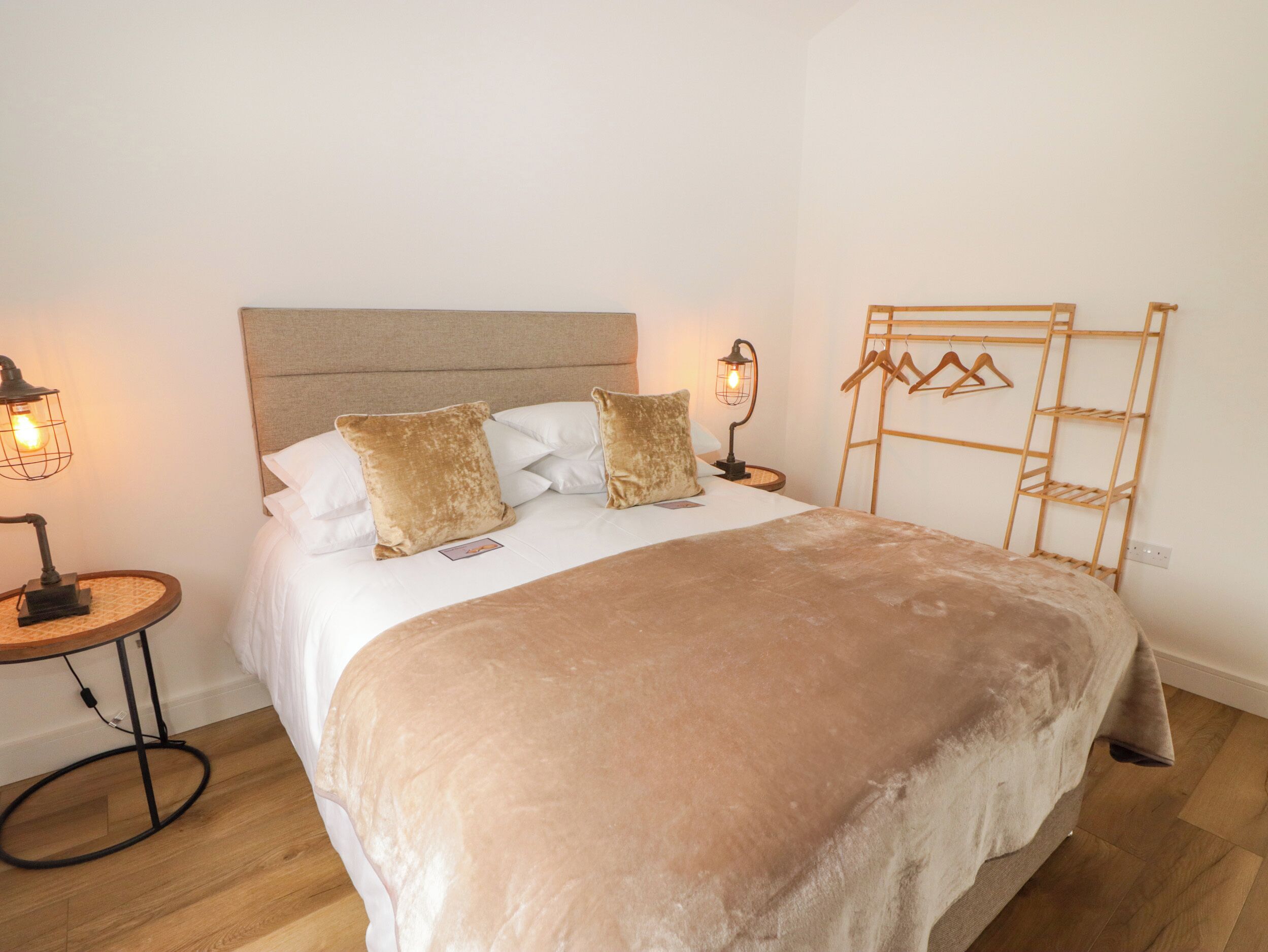 A neatly made bed with a beige blanket and pillows, two bedside lamps, and a wooden ladder shelf against the wall.