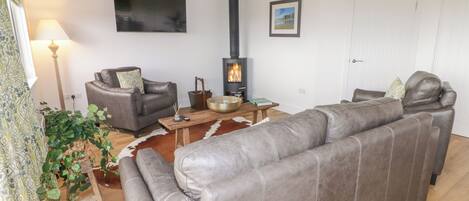 A living room with a sofa, two armchairs, a wooden coffee table, a fireplace, and a television mounted on the wall.