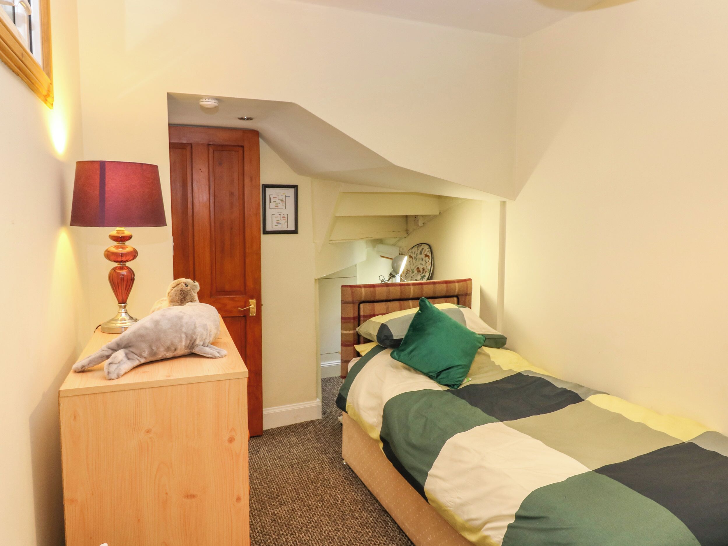 Un dormitorio con una cama, una mesita de noche de madera, una lámpara, una puerta y una lámpara de pared.