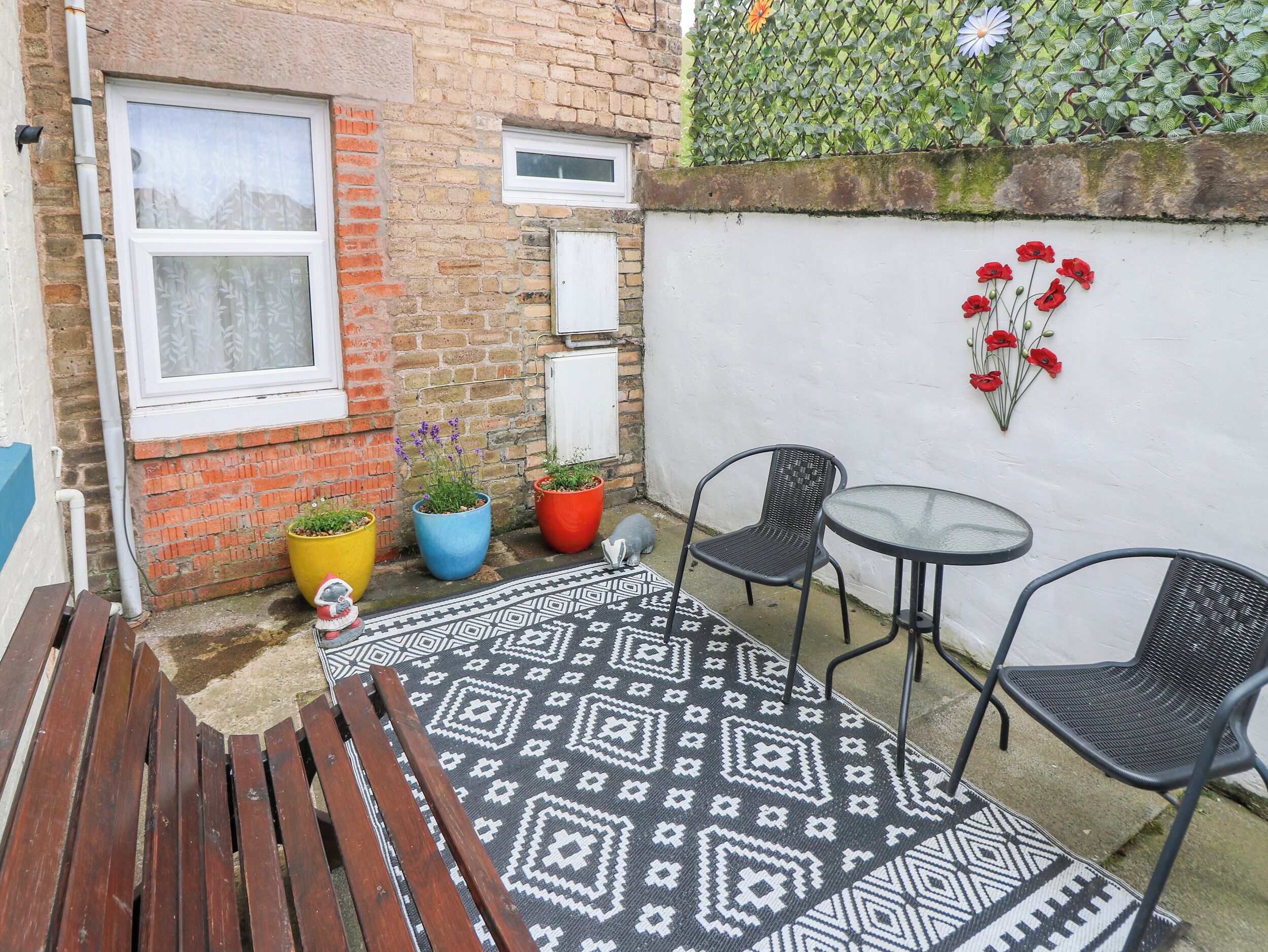 A small outdoor seating area with a patterned rug, a wooden bench, and a table with chairs.