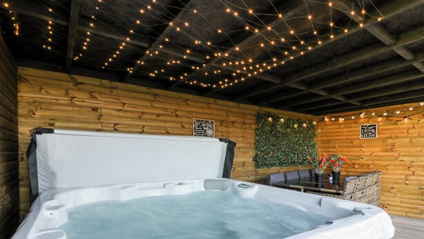 Un jacuzzi en una cabaña rústica con paredes de madera, luces de adorno y un cartel que dice "Eat Drink & Happy".
