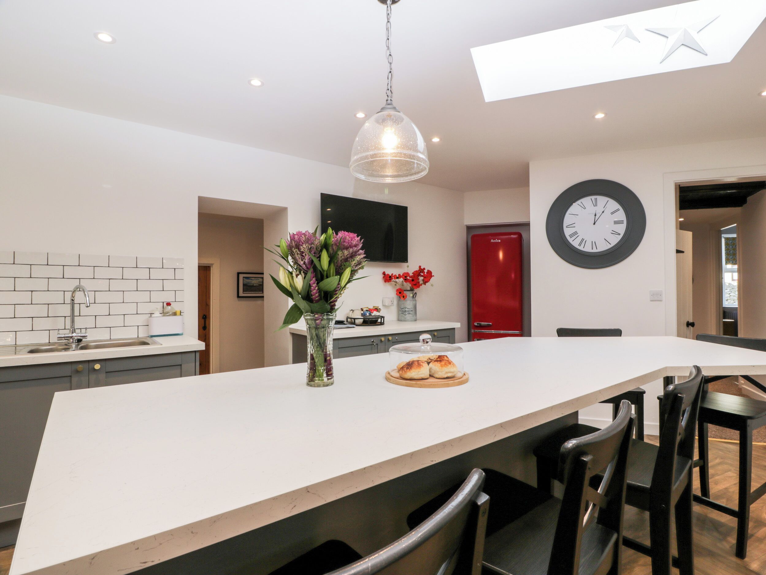 A modern kitchen with a large island, a red refrigerator, and a wall clock.