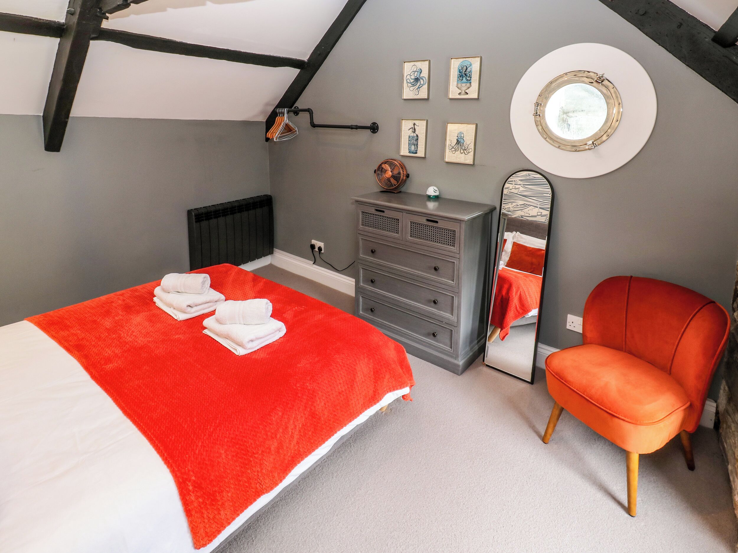 A bedroom with a bed, a dresser, a chair, a mirror, and artwork on the wall.