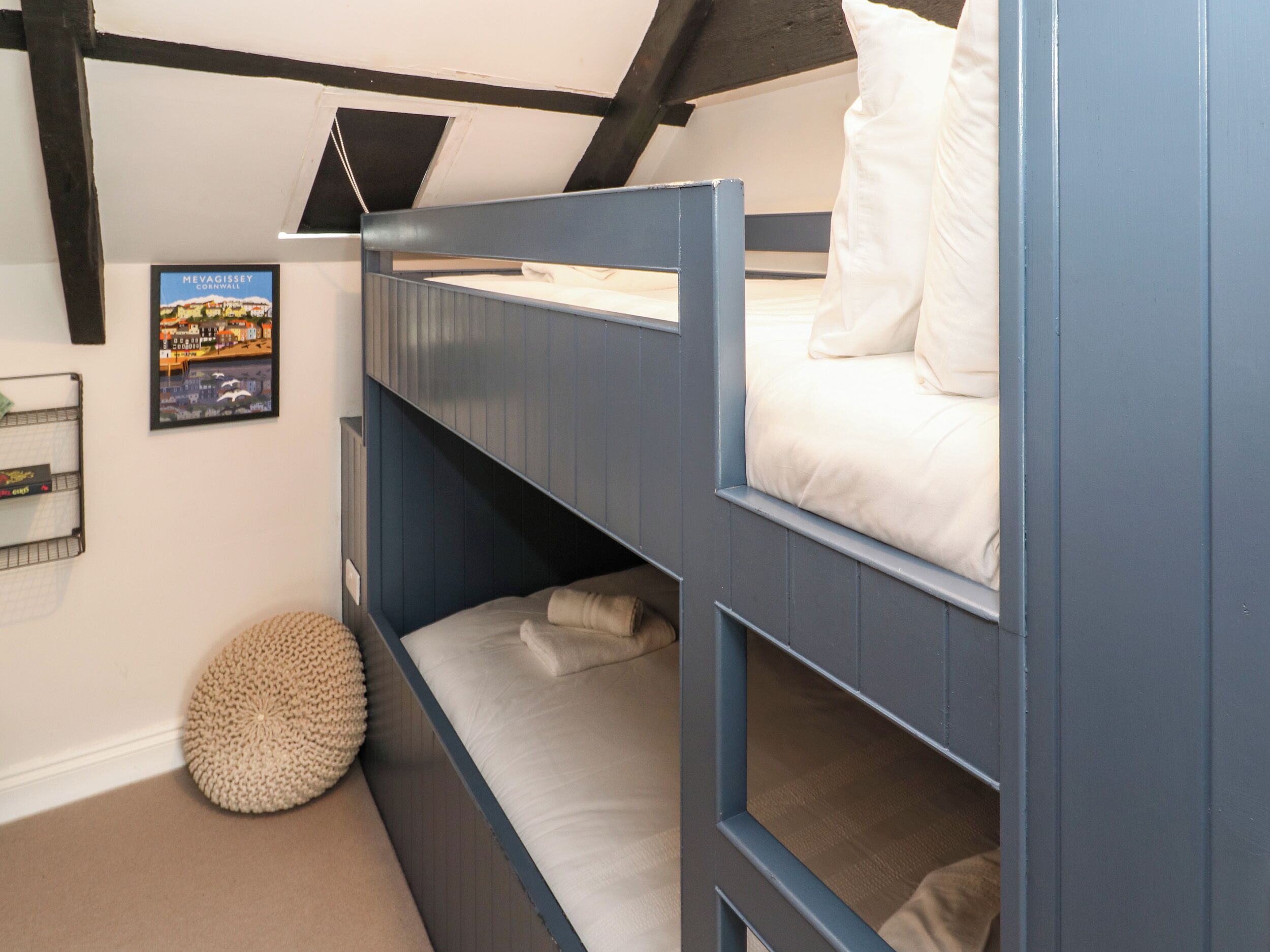 Una cama litera con una cama inferior y una superior, ambas con ropa de cama blanca. Encima de la cama, hay un cuadro enmarcado en la pared.