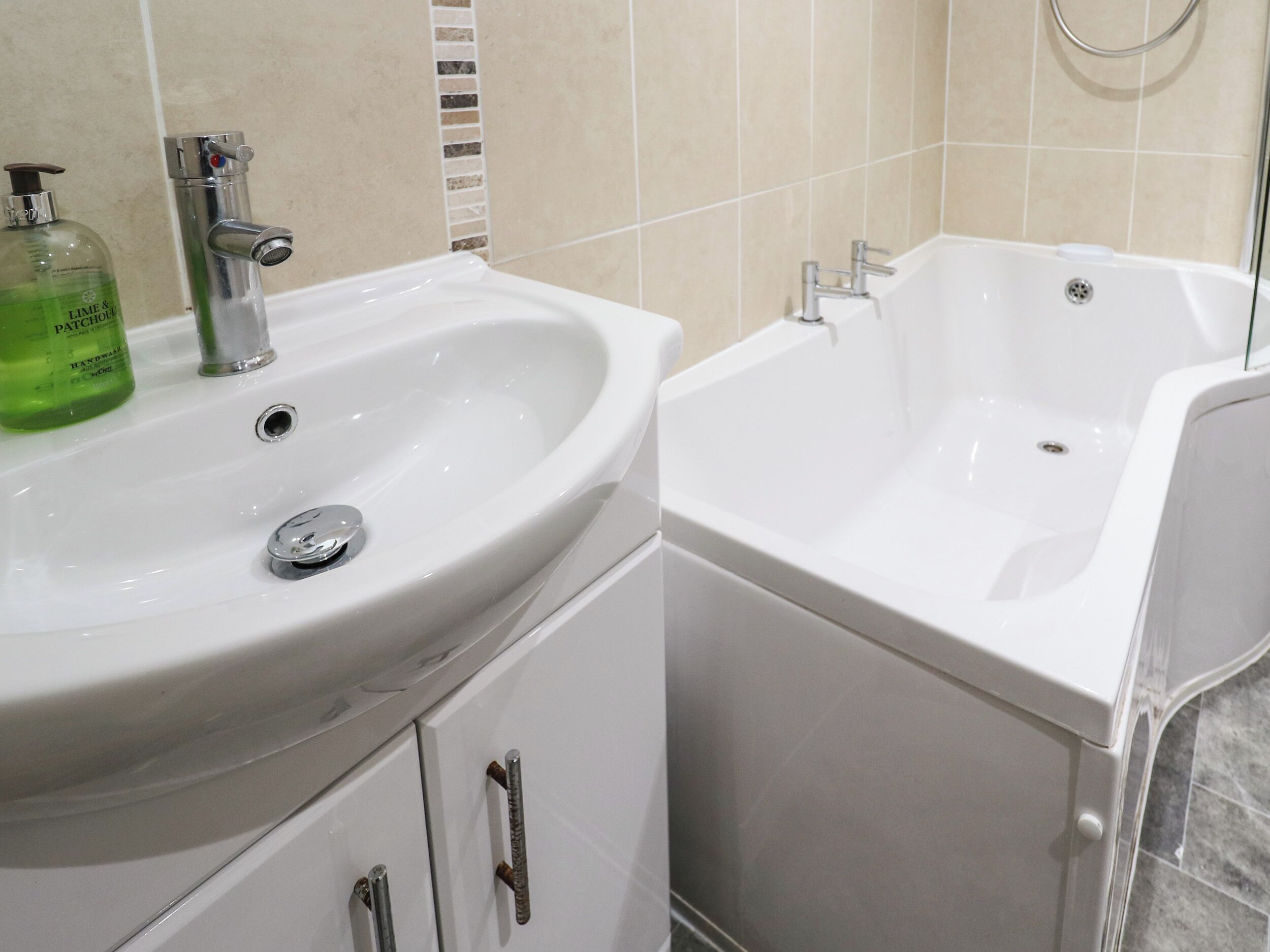 A bathroom with a white sink, a mirror, a green bottle of hand soap, and a white bathtub.