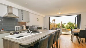 A modern kitchen with a central island, bar stools, and a dining area with a view. - Henham 3 Bernaleen Cottages (King's Lynn)