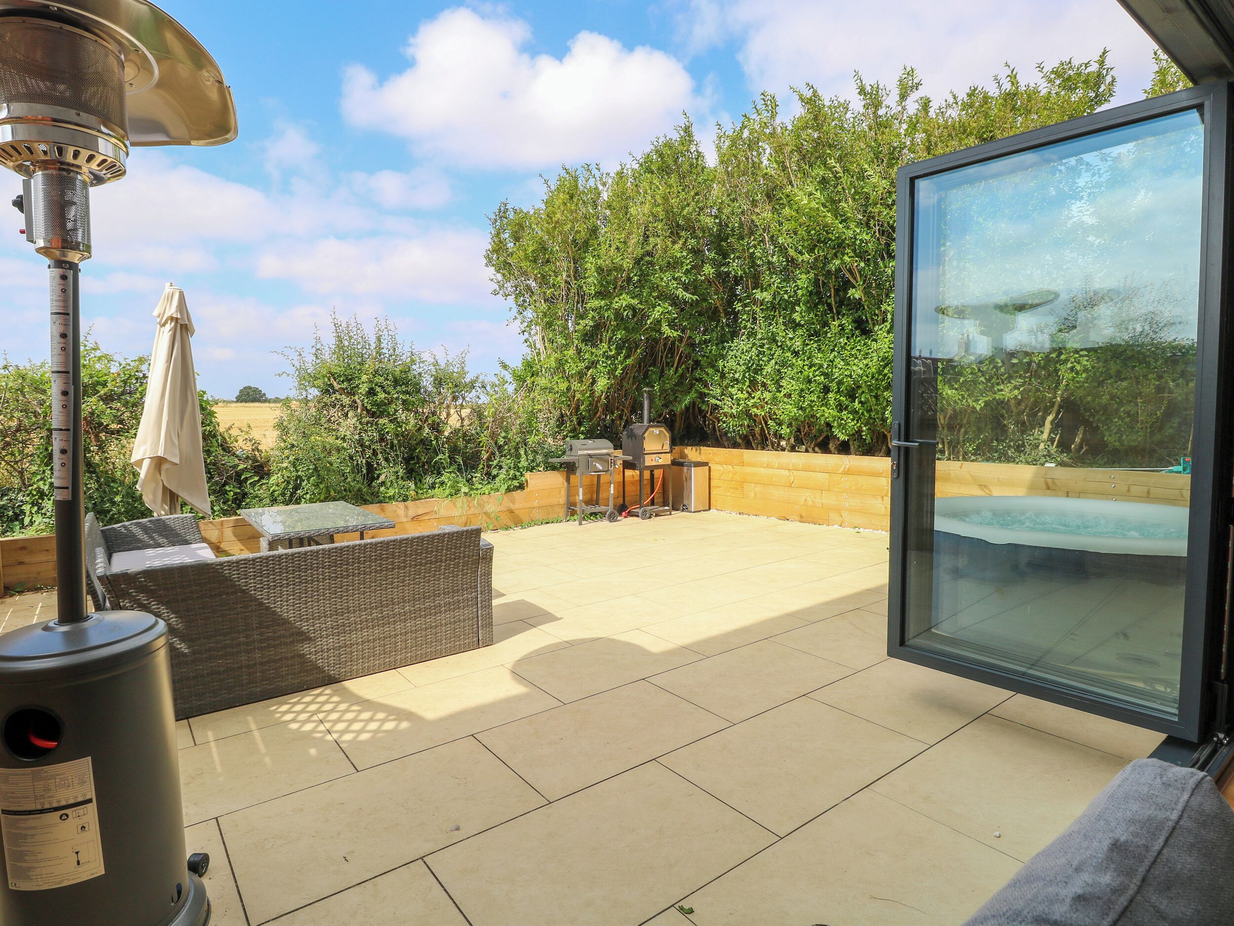 A patio with a glass door, wicker furniture, a grill, and a hot tub.
