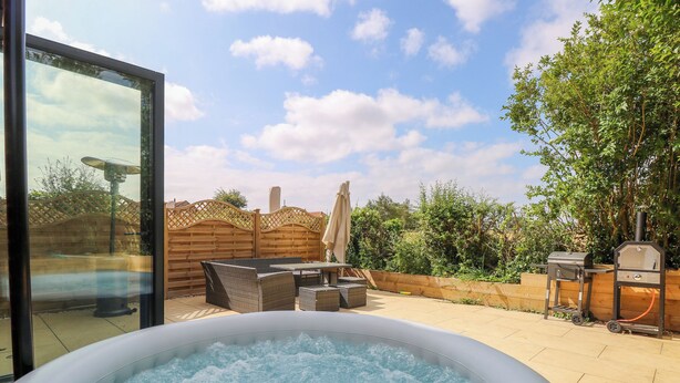 A hot tub in a backyard with a patio area, outdoor furniture, and a barbecue grill. - Henham 3 Bernaleen Cottages (King's Lynn)