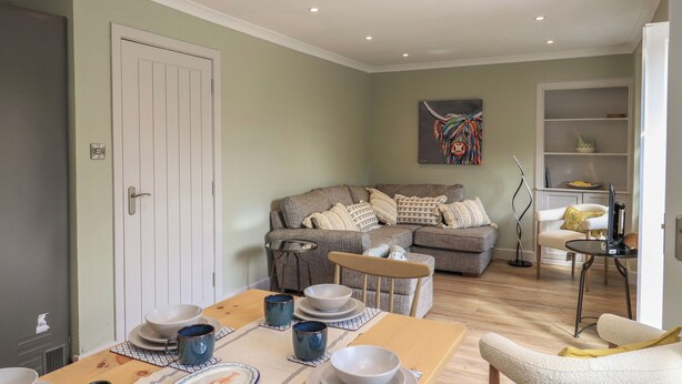 A dining area with a table set for four, a sofa, and a bookshelf. - 30 Northgate (Peebles)