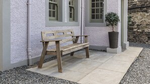 A wooden bench outside a building with stone walls and a potted plant. - 30 Northgate (Peebles)