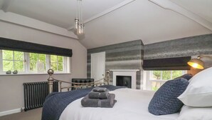 Een slaapkamer met een groot bed, een open haard, een radiator en een raam met uitzicht op groen.
