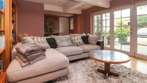 Een woonkamer met een beige hoekbank, een ronde salontafel en een pluizig vloerkleed.