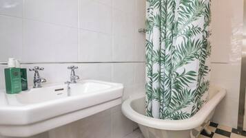 Um banheiro com pia branca, banheira estilo antigo e cortina de chuveiro com padrão de folhas.