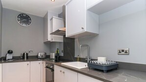 Een moderne keuken met witte kasten, een zwart aanrecht, een ingebouwde oven, een spoelbak met kraan en een klok aan de muur.