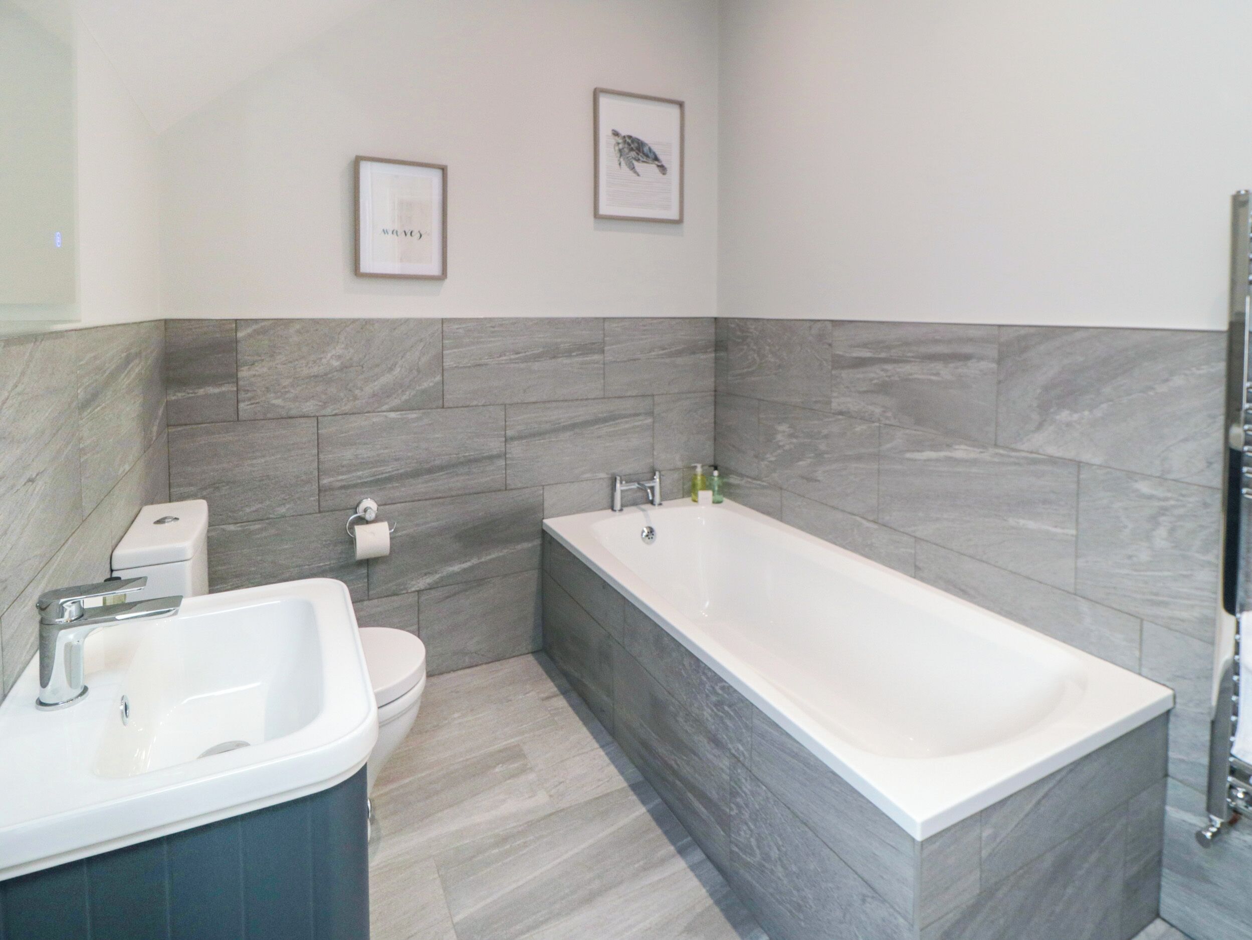 A modern bathroom with a bathtub, a sink, and a toilet. There are two framed pictures on the wall.